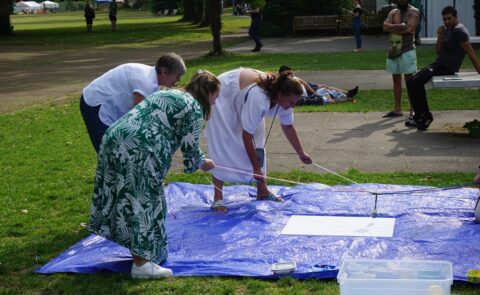 carmasec-Mitarbeitende beim gemeinsamen Teambuilding im Freien, drei Personen arbeiten konzentriert an einer Aktivität auf einer blauen Plane im Park