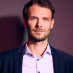 Lächelnder Mann mit rosa Hemd und schwarzer Jacke.
